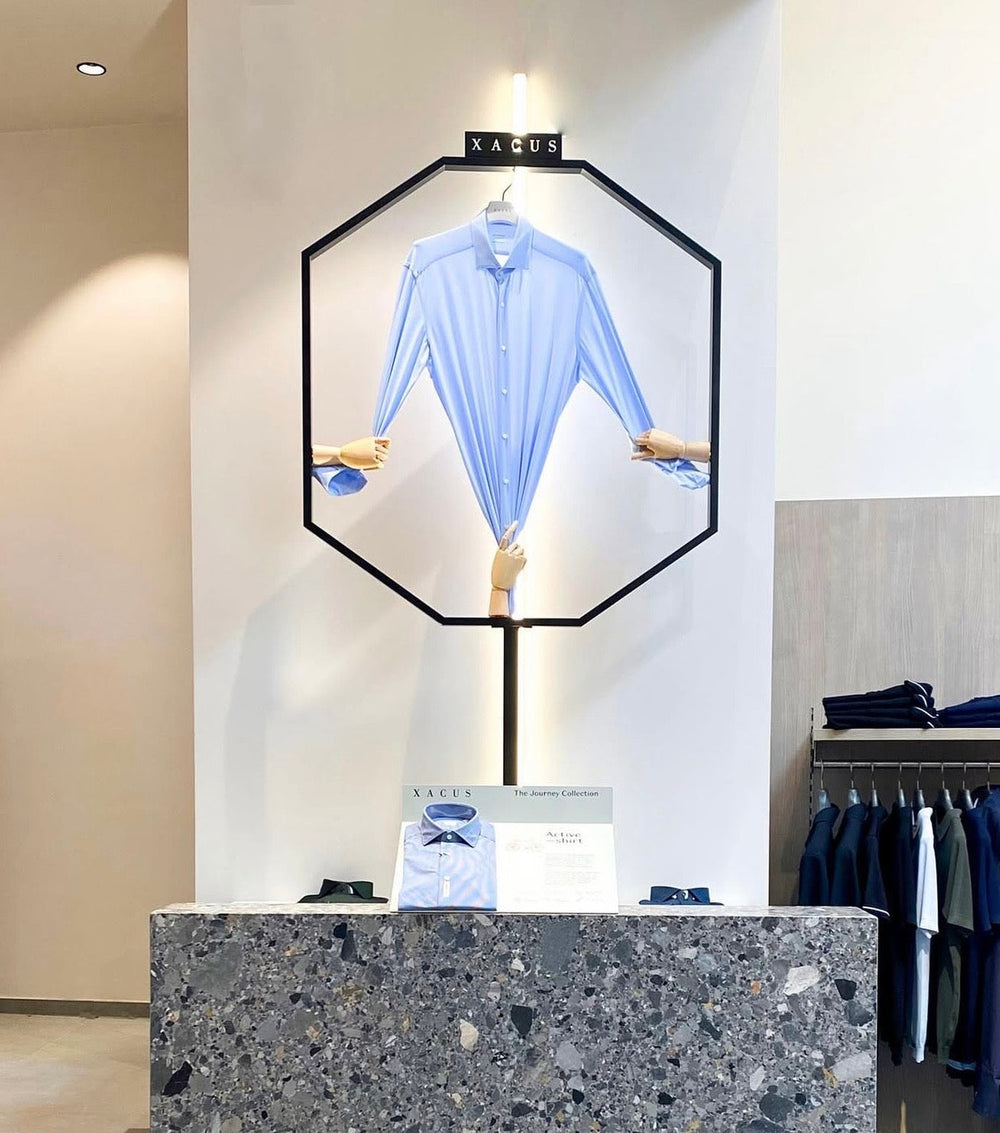 Lichtblauw Xacus Active Shirt uitgerekt door drie houten handen in de Xacus-presentatie bij Checkpoint Mol in Mol