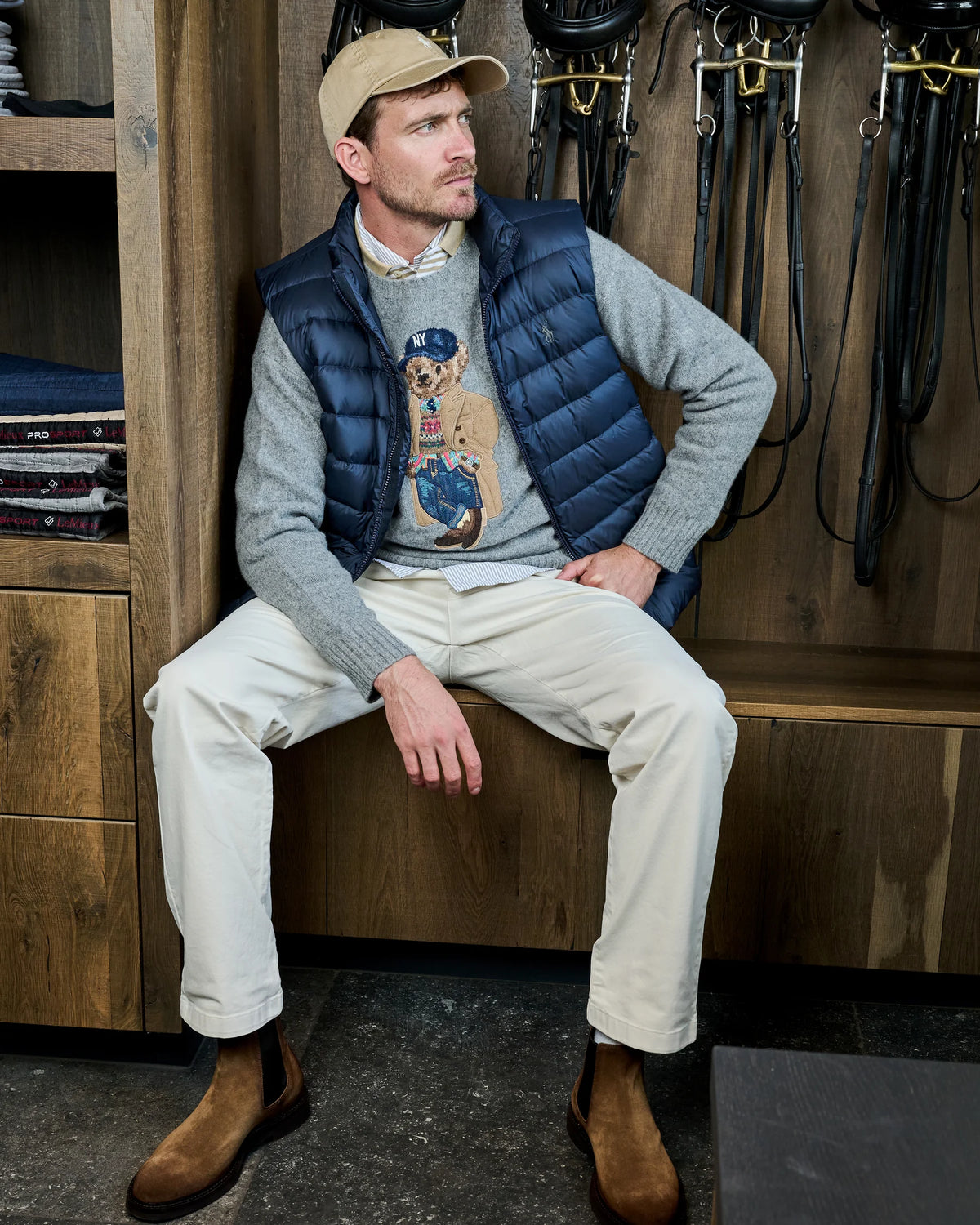 Grijze Ralph Lauren Polo Bear-trui met navy bodywarmer, ivory broek en suède Chelsea boots in de zadelkamer.