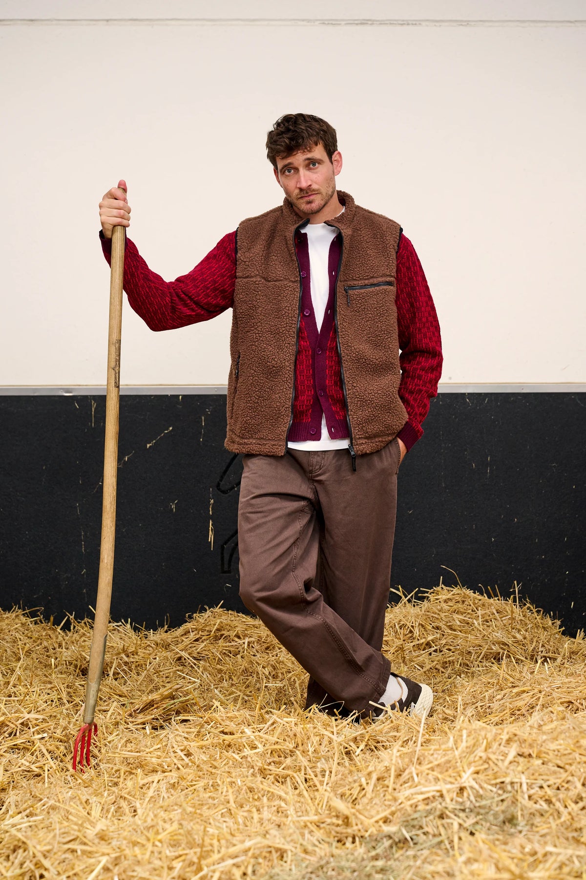 Herenlook met bruine bodywarmer, bordeaux cardigan en Gramicci broek tussen het hooi.