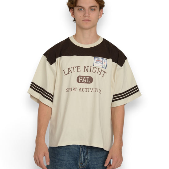 PAL Sporting Goods Late Night Sport T-shirt in Marshmallow en Deep Mahogany, gedragen vooraanzicht met borstprint en gestreepte mouwen.