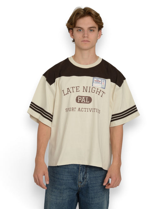 PAL Sporting Goods Late Night Sport T-shirt in Marshmallow en Deep Mahogany, gedragen vooraanzicht met borstprint en gestreepte mouwen.