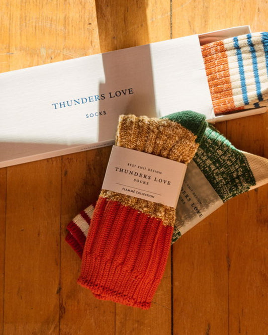 Thunders Love Cocktail Orange sokken naast andere sokken en Thunders Love-cadeaudozen op een houten tafel