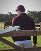 Bordeaux trui en pet met lichtblauw hemd aan de paddock voor de fotoshoot van Checkpoint Mol voor het Hidden Estate FW26 magazine op Begijnhoeve in Mol-Postel.